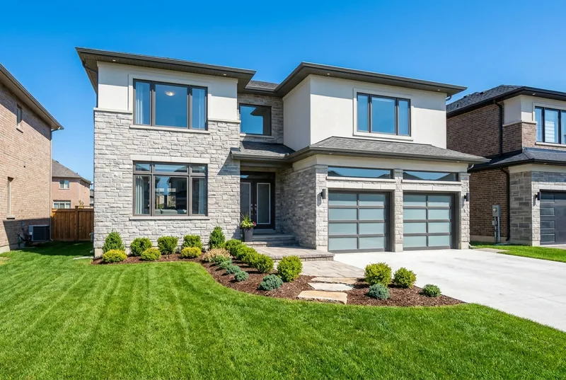 A sunny modern brick-and-stone two-storey family home with a green lawn under a blue sky.
