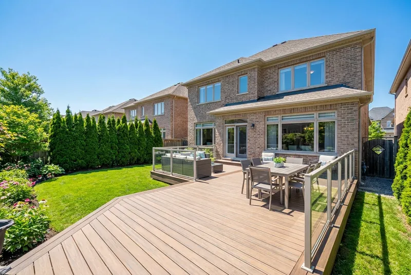 A sunny suburban backyard with a composite deck and glass railing.
