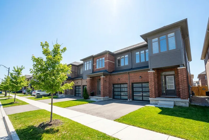 A bright brick freehold semi with a single garage and green yard on a sunny day.