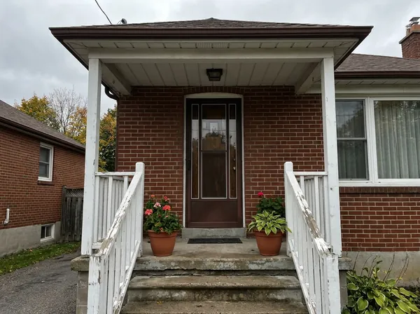 A modest brick home's covered front porch with potted plants.