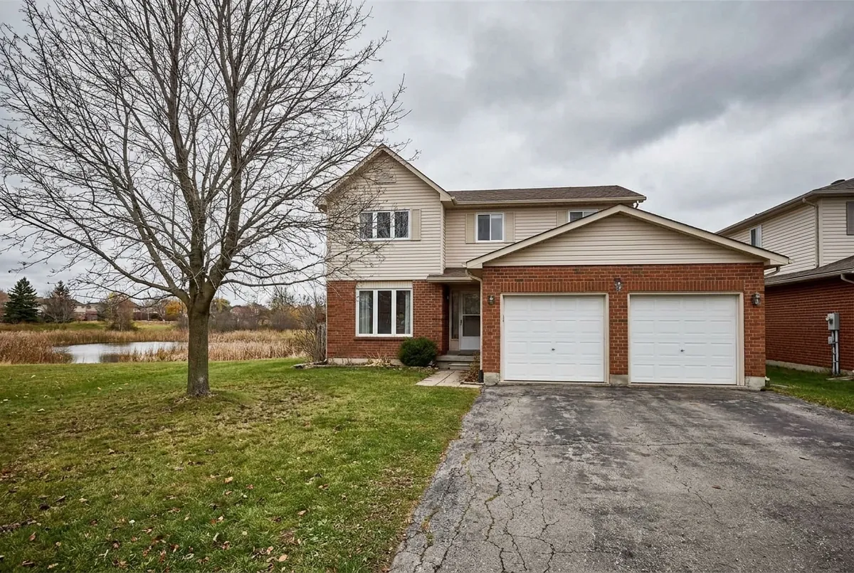 An ordinary Ontario brick-and-vinyl two-storey family home near the water under a grey sky.