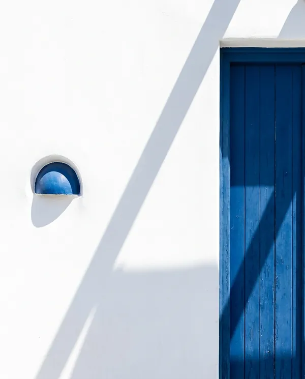 A white wall meeting a deep cobalt-blue door with one hard diagonal shadow.