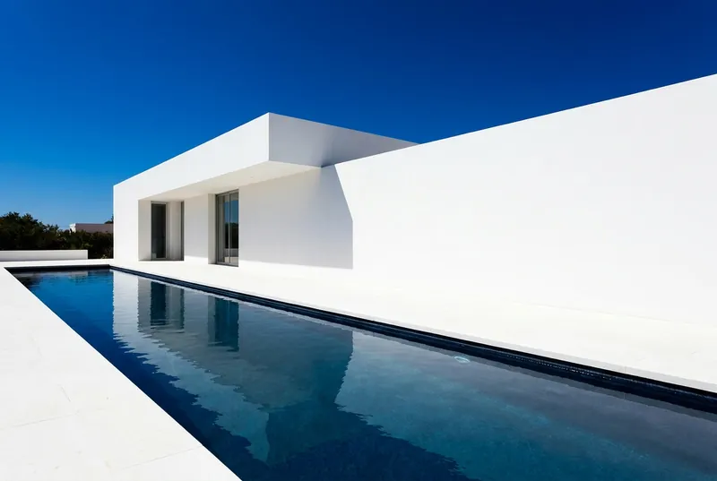 A white flat-roofed house with a long cobalt-blue lap pool.