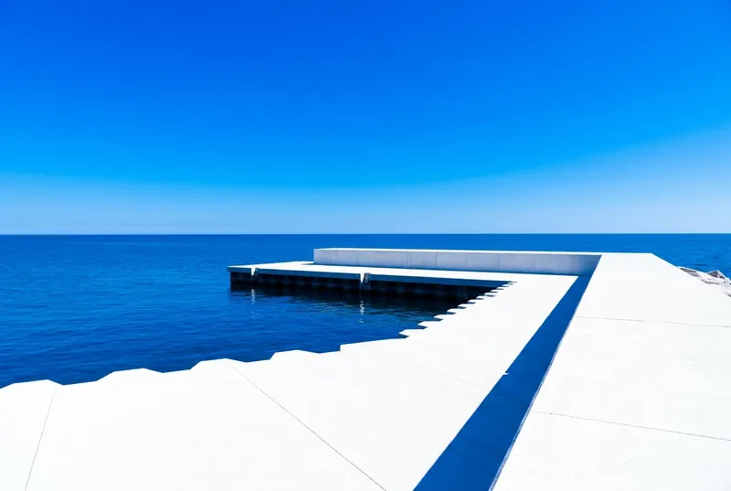 A clean white concrete breakwater reaching into deep blue Lake Ontario.