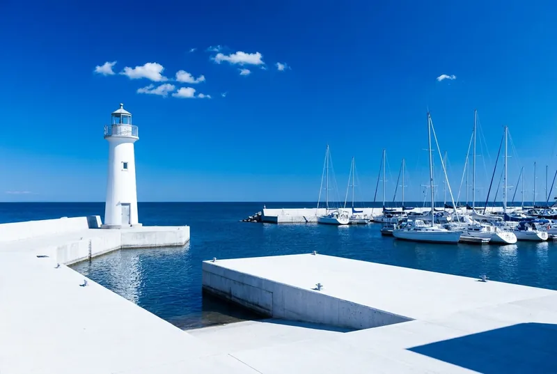 A white lighthouse and white sailboats at Port Credit on deep blue water.