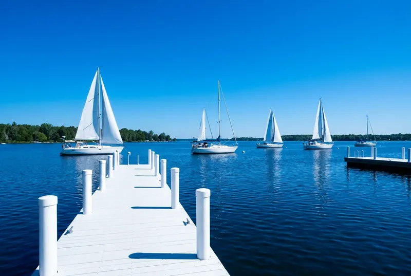 White sailboats on the deep blue Bay of Quinte beside a clean white dock.